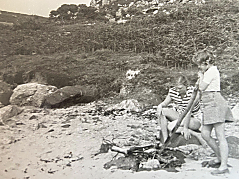 Children tending a bonfire on a Scottish beach with rocky hillside behind